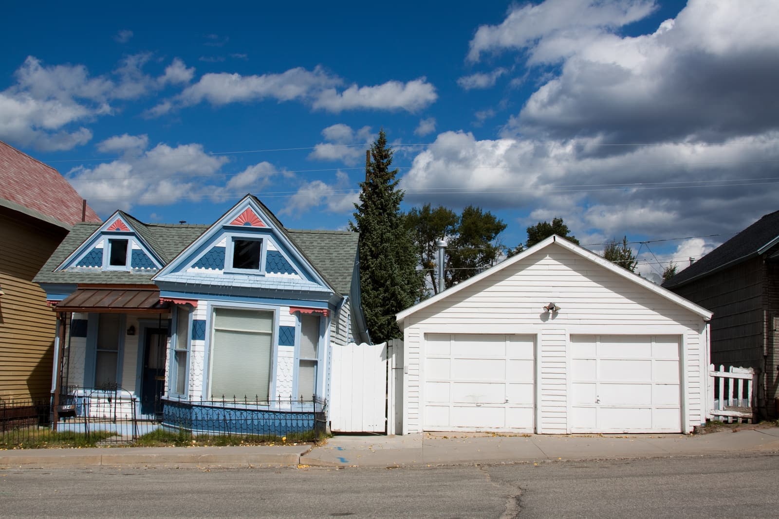A small Victorian-style home beside a detached garage under a wide blue sky